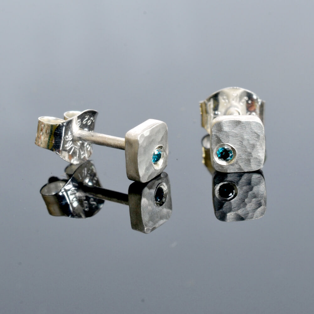 Hammered silver square studs with teal color enhanced blue diamonds. Handmade by EC Design using recycled metal and conflict-free stones.