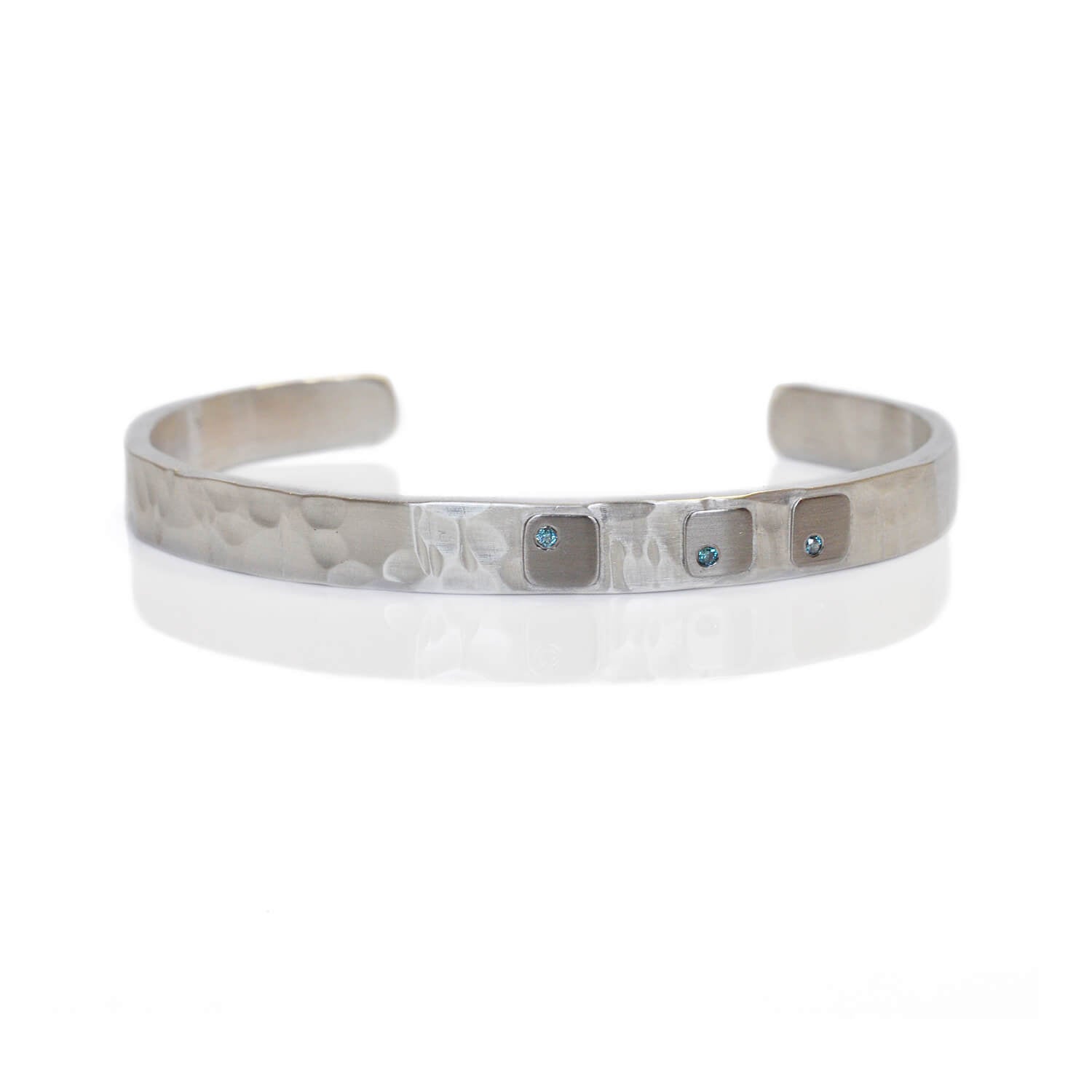 Sterling silver cuff with random hammered finish, palladium cell accents, and 3 flush set blue diamonds.